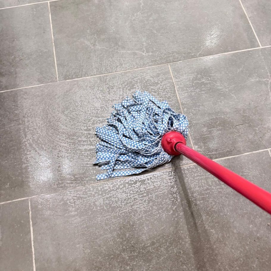 Wischmopp auf Fliesenboden mit sichtbaren Wasserschlieren